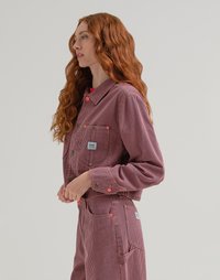 Giacca corta a righe rosse e bianche con due tasche frontali, chiusura con bottone e patch con logo; abbinata a pantaloni a righe coordinati.