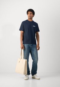 Mørkeblå bomull T-skjorte med korte ermer, lyseblå denimjeans og en kremfarget kanvas totebag, kombinert med hvite sneakers.