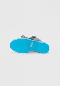Gray shoe with a blue rubber sole. The sole features a textured finish and branding, and the upper portion is made of soft material.