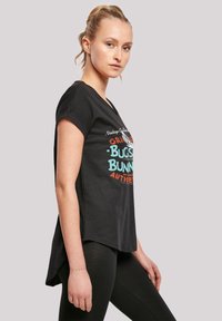 Svart T-skjorte med grafisk design som har teksten "Bugs Bunny" i oransje og turkis. Korte ermer, buet kant og mykt stoff.