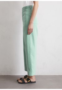 Pantalons à larges jambes vert menthe en tissu doux, dotés de poches avant et arrière. Associés à des sandales noires avec une boucle dorée.