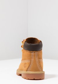 Brune læder ankelstøvle med gule snørebånd, polstret brun krave, kontrasterende hvid syning og en struktureret gummisål. Timberland-logoet er synligt.