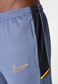 Nike atletske kratke hlače od lagane plave tkanine s crnim detaljima, sa vezanom žutom logotipom i bočnom džepom.