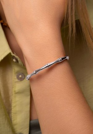 Bracciale d'argento con un design ispirato al bambù, che presenta segmenti cilindrici lisci e una lucentezza sottile. Indossato su un polso.