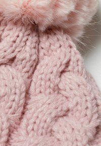 Pink knitted beanie featuring a cable knit pattern, with a fluffy pink pom-pom on top. Soft texture with thick yarn.