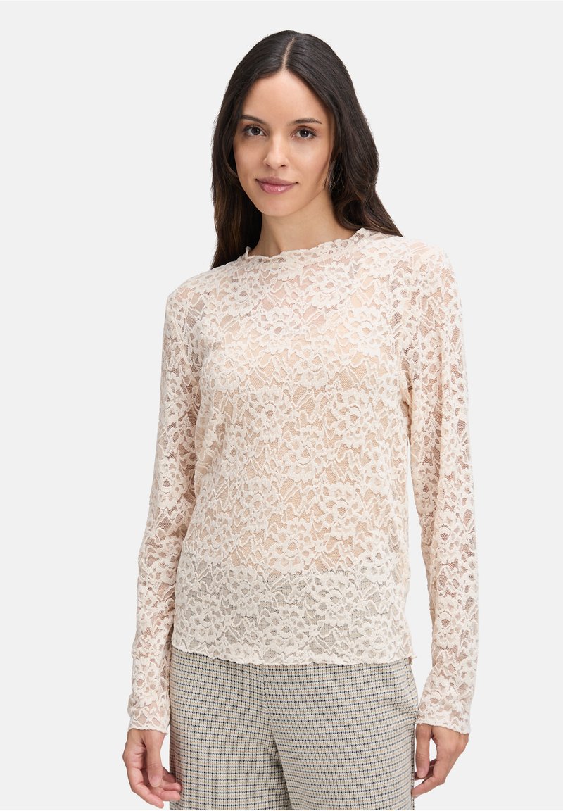 Lange mouwen kanttop in lichtbeige met bloemenpatroon, ronde halslijn en gegolfde randen, gecombineerd met geblokte broek.