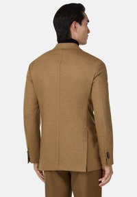 Pruun kohandatud bleiser struktureeritud õlgadega, ühe lõhiku ja nööpidega mansettidega. Sile tekstuur, elegantne siluett ja minimalistlik disain.