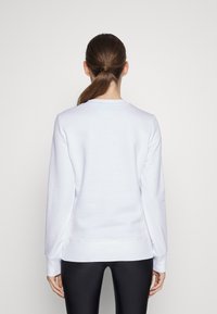 Felpa bianca con maniche lunghe, collo rotondo, texture liscia e polsini a coste, abbinata a leggings neri. Vista posteriore mostrata.