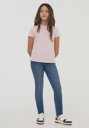 T-shirt rosa a maniche corte abbinata a jeans slim-fit blu e sneakers marroni e bianche. La maglietta ha un collo rotondo e una vestibilità comoda.