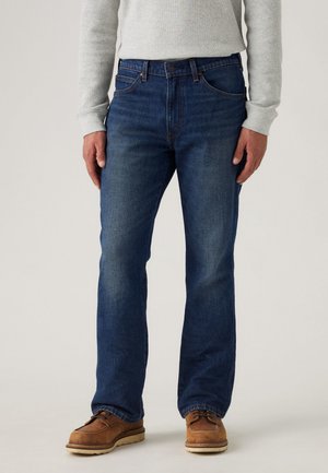 Dunkelblaue Jeans aus Denim mit geradem Bein, auffälligen Nähten und einem klassischen Fünf-Taschen-Stil. Tragen mit braunen Lederschuhen.