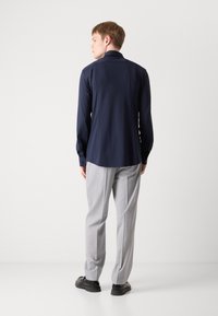 Camisa de manga larga azul marino con cuello puntiagudo y puños de botón, acompañada de pantalones gris claro. Tejido suave y elegante con una silueta estructurada.