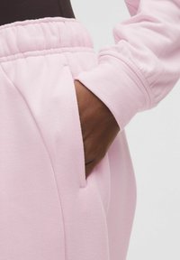 Világos rózsaszín sportnadrág, rugalmas derékkal, oldalsó zsebbel és puha, texturált anyaggal a kényelem érdekében.