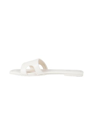 Sandalo piatto bianco con ampio cinturino caratterizzato da un design traforato e suola sottile, visto di profilo su sfondo bianco.
