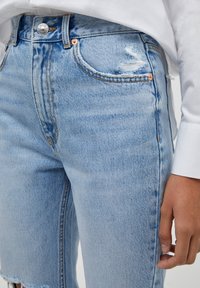 Lichtgewassen denim jeans met een versleten textuur, voorzien van oranje stiksel en een hoge taille, met zichtbare zakken en franje aan de broekspijpen.