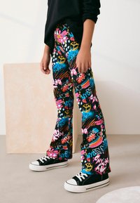 Svarta utsvängda byxor med ett färgglatt graffiti-inspirerat mönster, med olika ljusa designer och motiv. Matchas med svarta sneakers.