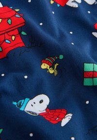 Snoopy w niebieskiej zimowej czapce i czerwonym szaliku na niebieskiej tkaninie z Woodstockiem w pasiastym kapeluszu, światełkami świątecznymi i pudełkiem na prezent.