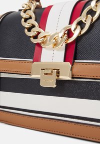 Struktureret håndtaske med sorte, hvide og røde striber, guld kæde hardware og en rektangulær lås med en tan accent.
