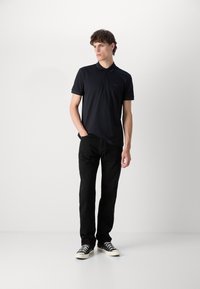 Μαύρο πόλο μπλουζάκι με κοντά μανίκια και διακριτικό λογότυπο, συνδυασμένο με μαύρα τζιν με ίσια γραμμή και μαύρες καμβά υφασμάτινες sneakers με λευκή σόλα.