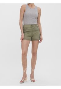 Shorts en dentelle vert olive avec taille à cordon, ourlet festonné, associés à un débardeur gris et des talons beiges à brides. Texture lisse.