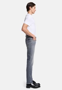 Grijze slim-fit jeans met een vervaagd effect, vijf zakken en zwarte accenten, gecombineerd met een wit T-shirt en zwarte veterschoenen.