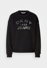 Svart hettegenser med "DKNY 1989 JEANS" i sølvfarge. Laget av myk stoff, med ribbestrikkede mansjetter og hem. Rent, uformelt design.