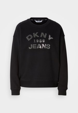 Black sweatshirt featuring "DKNY 1989 JEANS" in silver lettering. Made of soft fabric, with ribbed cuffs and hem. Clean, casual design.