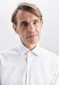 Een knoopsluiting shirt in frisse witte stof, met een puntige kraag en een gladde textuur. Het onderwerp heeft kort, licht verward haar en lichte ogen.