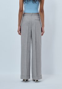 Grey, wide-leg trousers with a smooth texture and a tailored fit. Features a back pocket, cuffed hems, and a mid-rise waistband.