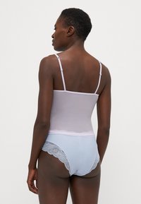 Camisola lilla con spalline sottili abbinata a biancheria intima azzurra con pizzo lungo i bordi, tessuto liscio e design aderente.