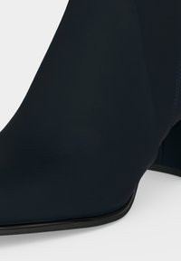 Gros plan d'une bottine noire à bout carré et talon carré sur fond blanc.