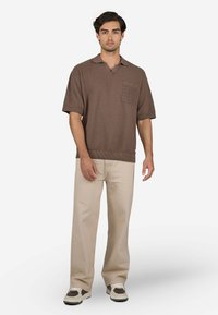 Braunes kurzärmeliges Polohemd mit einer strukturierten Tasche, kombiniert mit hellbeigen Hosen und Turnschuhen mit braunen Akzenten.