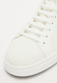 Sneaker bianco con sopra in rete testurizzata e dettagli in pelle liscia. Caratterizzato da lacci bianchi piatti e una suola in gomma con orlo cucito.
