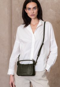 Borsa a tracolla in pelle verde scuro con finitura texturizzata, dettagli con manico annodato e tracolla regolabile. Design rettangolare compatto.