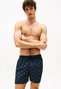 Marineblå svøm shorts med elastisk talje, der har små hvide geometriske mønstre. Lavet af letvægtsstof, egnet til vandaktiviteter.