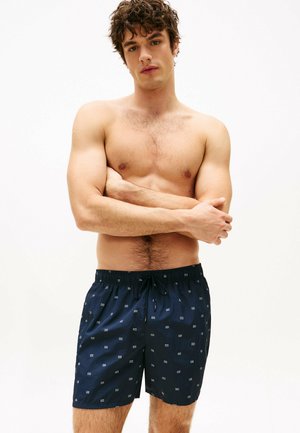 Marineblaue Schwimmshorts mit elastischem Bund, verziert mit kleinen weißen geometrischen Mustern. Hergestellt aus leichtem Stoff, geeignet für Wasseraktivitäten.