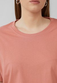 Różowa bawełniana koszulka z okrągłym dekoltem i krótkimi rękawami. Gładka tekstura, minimalistyczny design i brak widocznych wzorów lub akcentów.