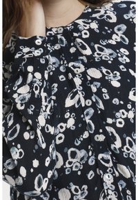 Svart- och vitt mönstrad skjorta med en texturerad tygkvalitet, med knappr detaljer vid ärmsluten och rund halsringning. Cirklar och detaljer i olika storlekar.