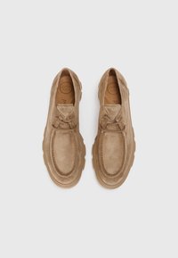 Chaussures en suède beige avec une pointe arrondie, des détails de couture proéminents et une semelle en caoutchouc épaisse, dotées de lacets et d'une finition texturée.
