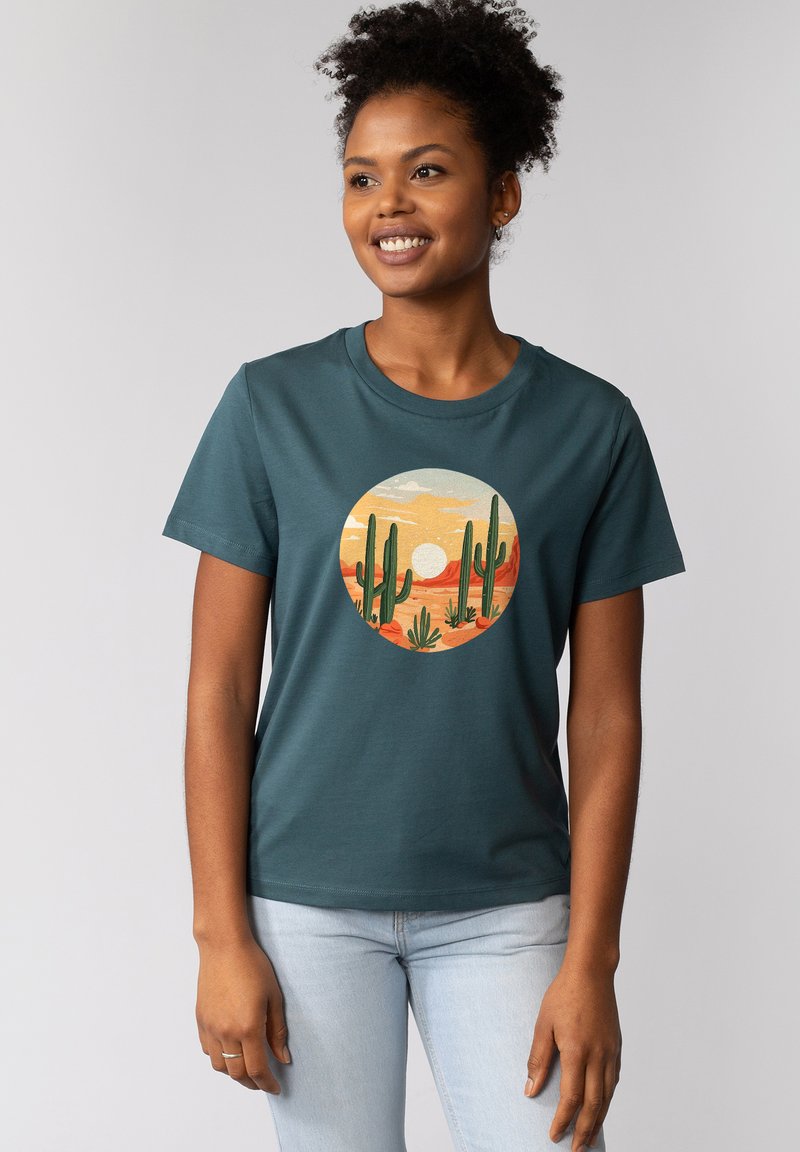 Teal katoenen T-shirt met een ronde grafische print van cactussen en een zonsondergang in oranje en beige tinten. Korte mouwen en een ronde hals.