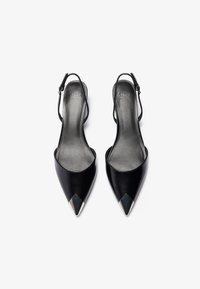 Crne lakirane slingback pete s šiljastim čarapama i metalnim naglascima. Glatka tekstura, podesiva traka i minimalni dizajnerski detalji.