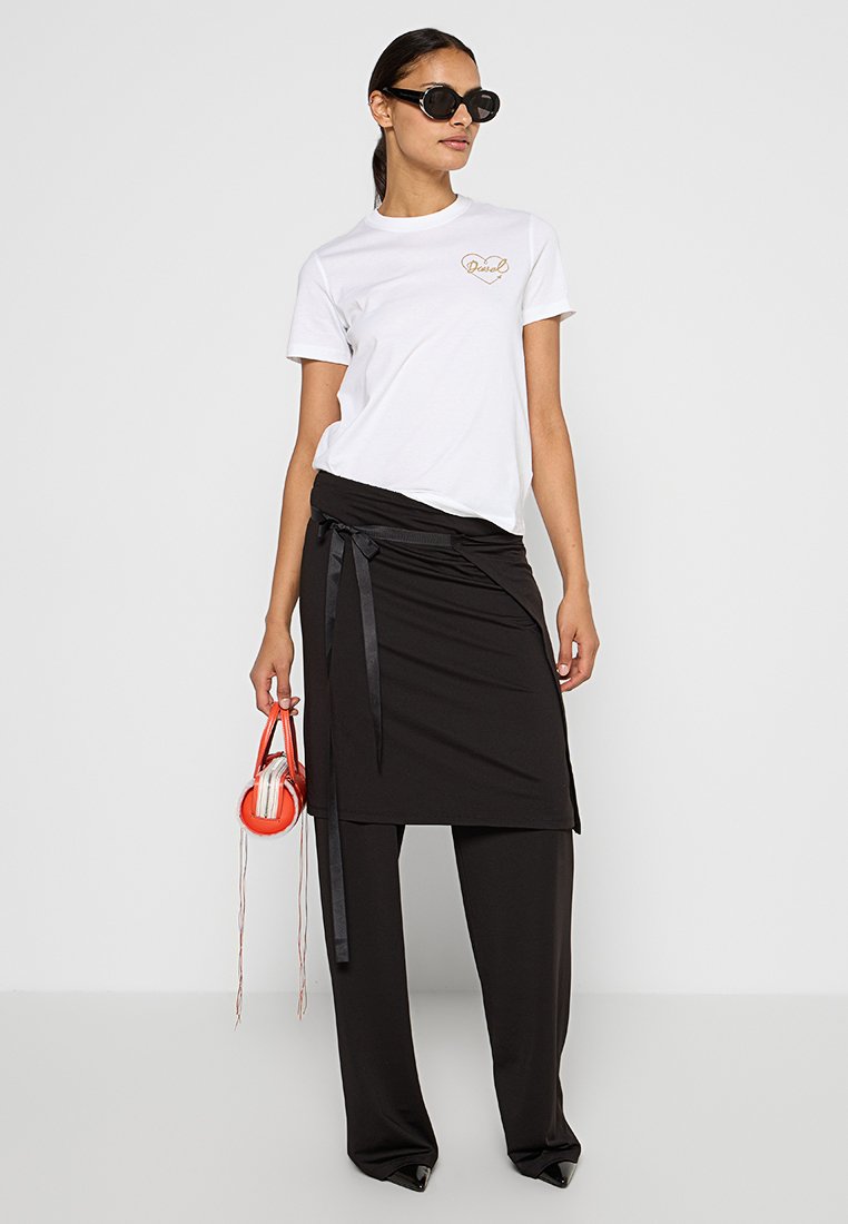 Biała koszulka z złotym sercem, zestawiona z czarną spódnicą kopertową z kokardą, czarnymi szerokimi spodniami i małą czerwoną torebką.