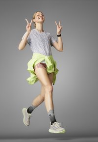 Camiseta deportiva gris con patrón, pantalones cortos rosas y una chaqueta verde neón atada a la cintura. Zapatillas gris claro con detalles verdes y calcetas a rayas.