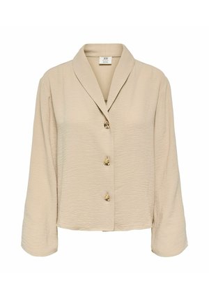 Blouse beige à manches longues en tissu texturé, avec trois boutons dorés sur le devant et un large col à revers.