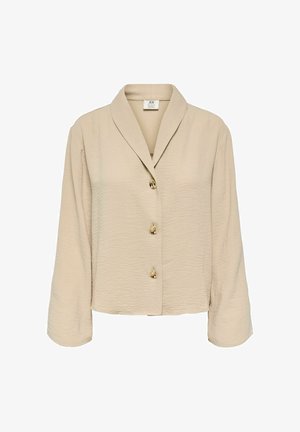 Blouse beige à manches longues en tissu texturé, avec trois boutons dorés sur le devant et un large col à revers.