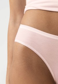 Sous-vêtements en coton rose clair avec une texture lisse, présentant une coupe taille basse et une ceinture élastique douce. Design simple sans motifs.