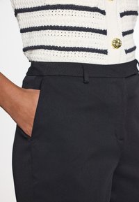 Svarta skräddarsydda byxor med en slät yta, utrustade med sidfickor och en platt framdel, kombinerade med en vit och marinblå randig stickad tröja.