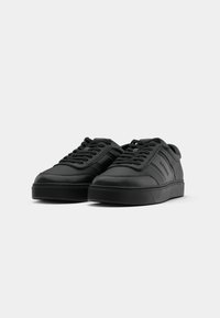 Black leather sneakers with textured design, round toe, padded tongue, and flat rubber sole. Features tonal stitching and lace-up closure.