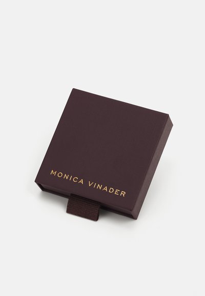 Boîte à bijoux en cuir brun texturé avec un logo doré "MONICA VINADER" et une languette. Design carré avec une finition lisse.