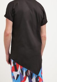 Camisa negra de manga corta con dobladillo curvado, hecha de una tela suave, combinada con pantalones cortos azul de estampado atrevido que presentan formas geométricas rojas y blancas.