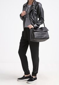 Czarna skórzana kurtka na szarej koszulce z logo, dobrana do czarnych zwężanych spodni i czarnych butów wsuwanych. Duża czarna torebka o fakturowanej powierzchni.